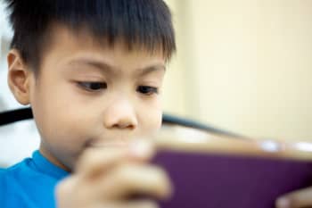 A child holds a mobile phone with both hands and looks intently at the screen.