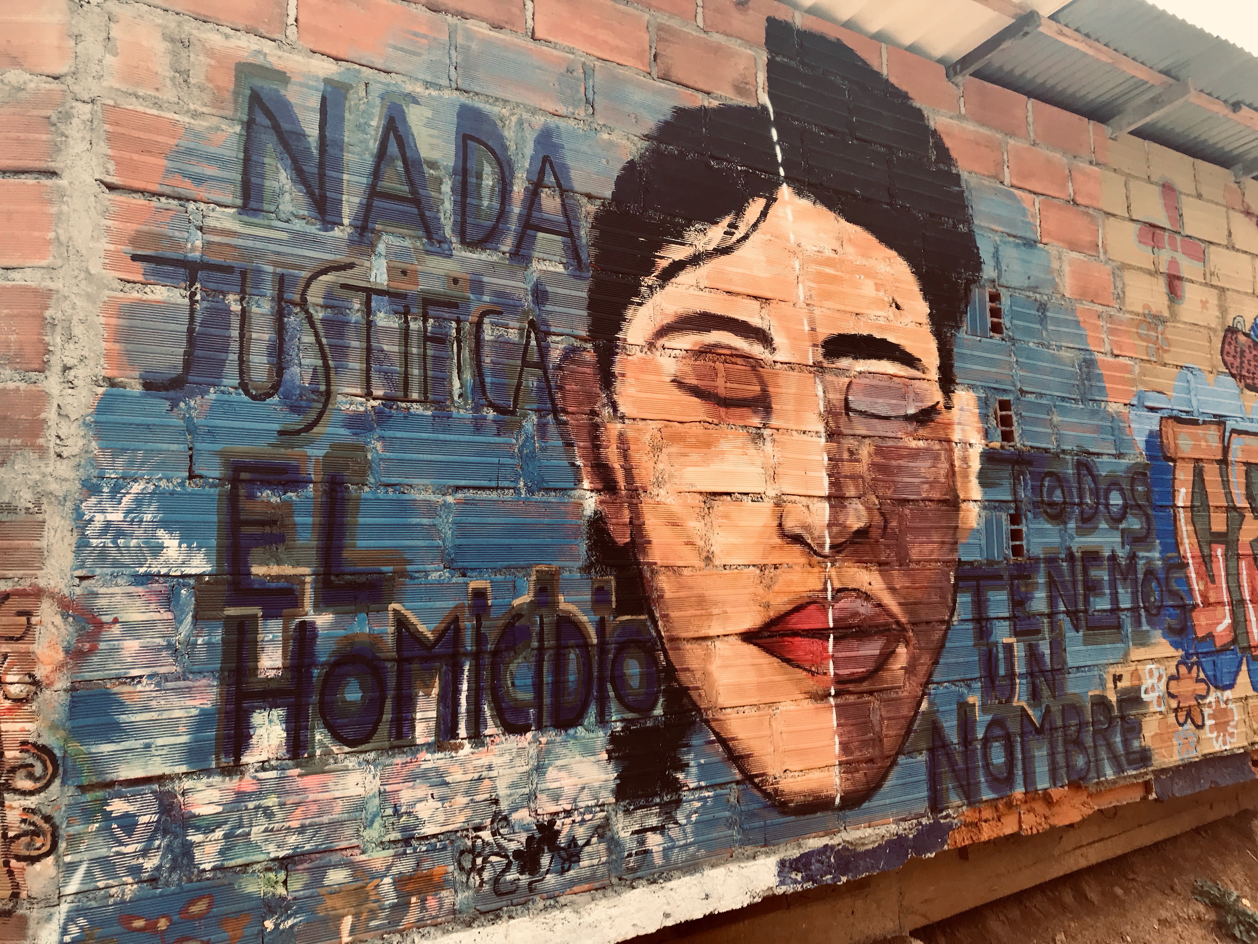 A street art mural in Colombia with a person's face with their eyes closed, surrounded by the words "Nada justifica el homicidio - todos tenemos un nombre"