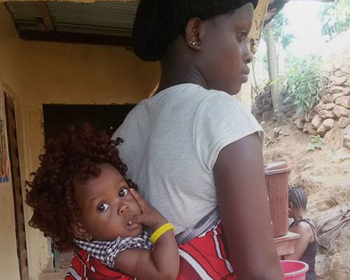 Photo of an infant wearing one of the color-coded bracelets while strapped to their mother's back.