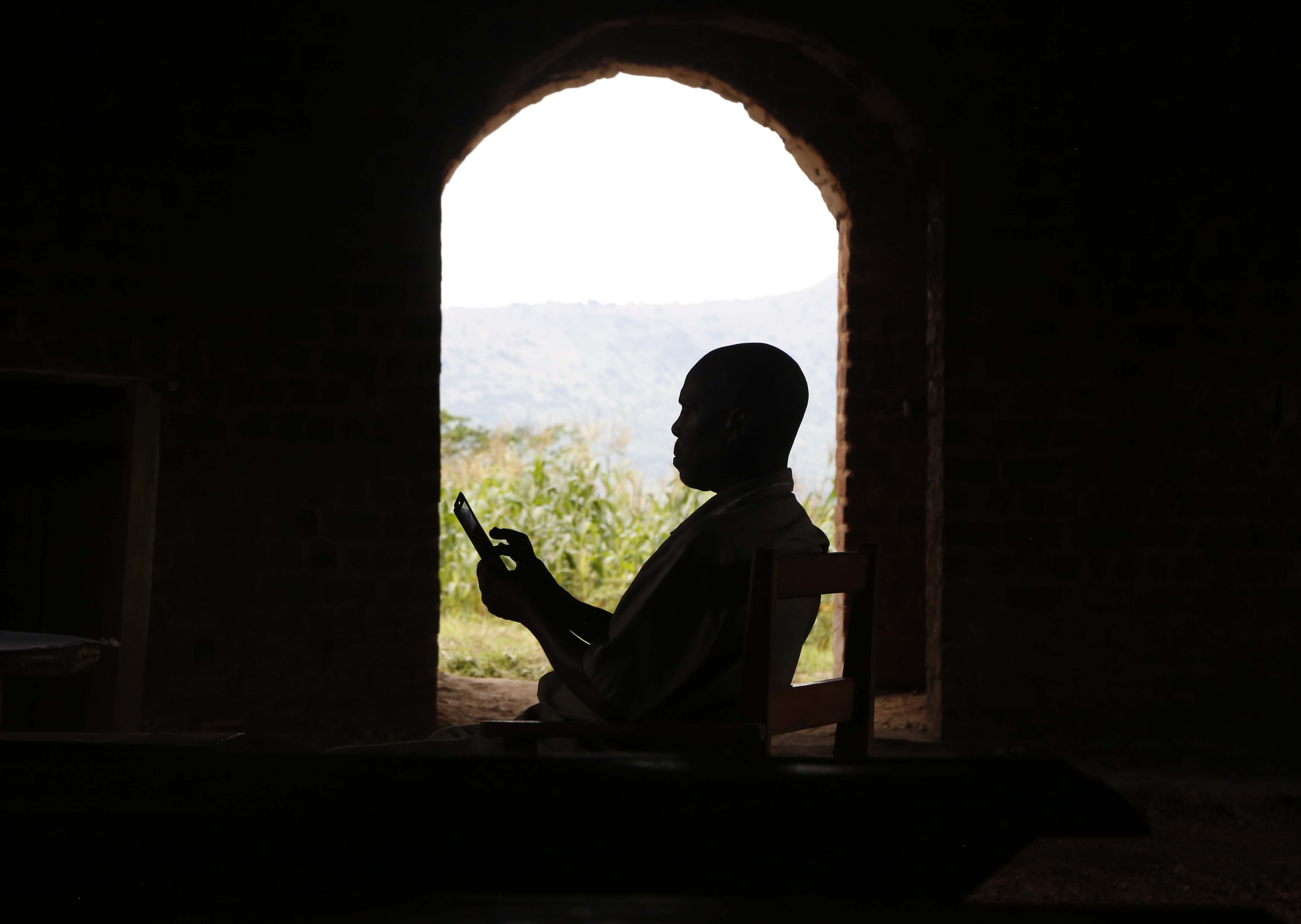 A silhouette in shadow of a faith leader sitting in a church reading from his phone in his hand