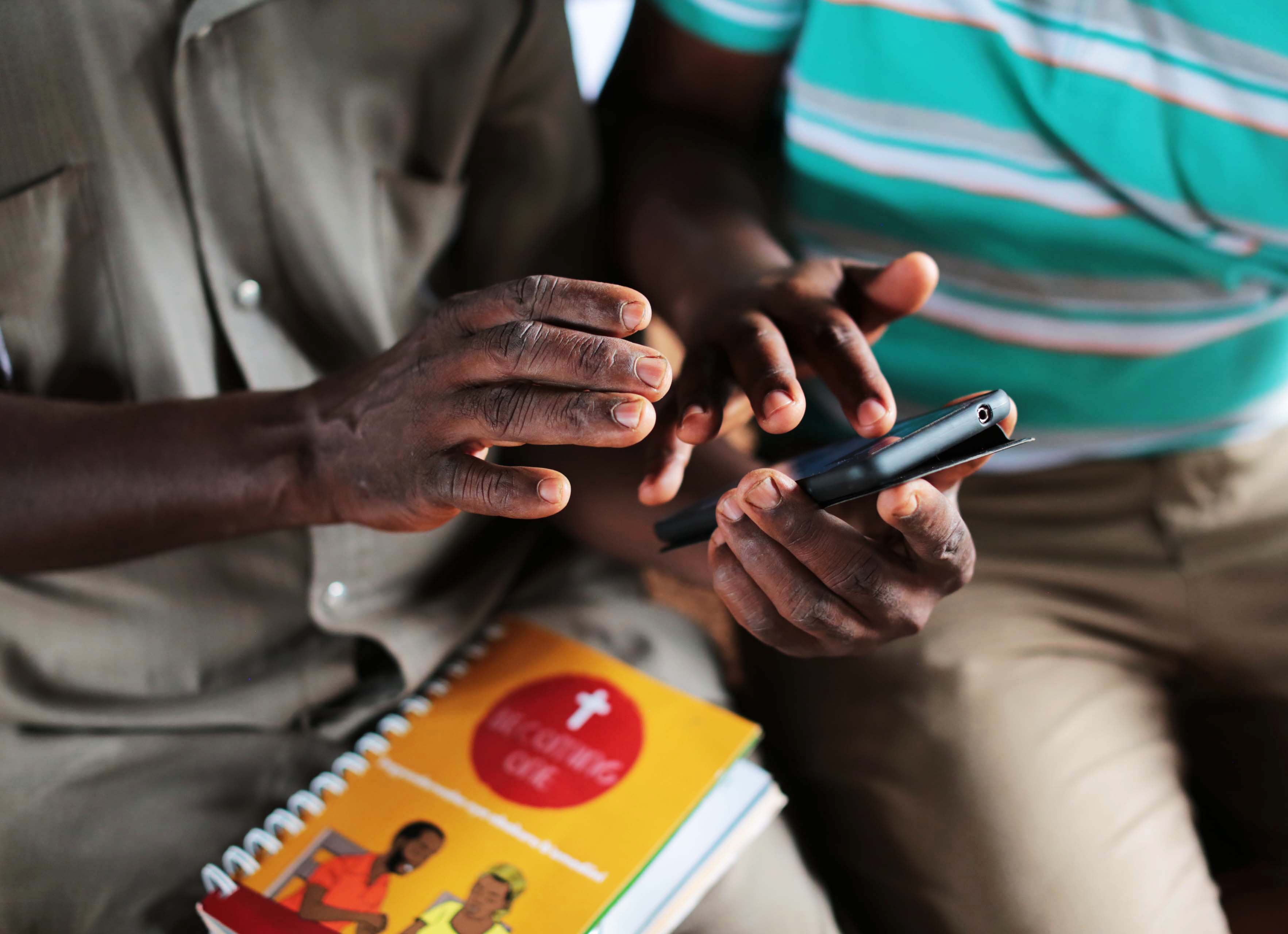 A close-up of the Becoming One curriculum notebook placed on the lap of a faith leader, who is sitting next to an IPA enumerator on the Becoming One project