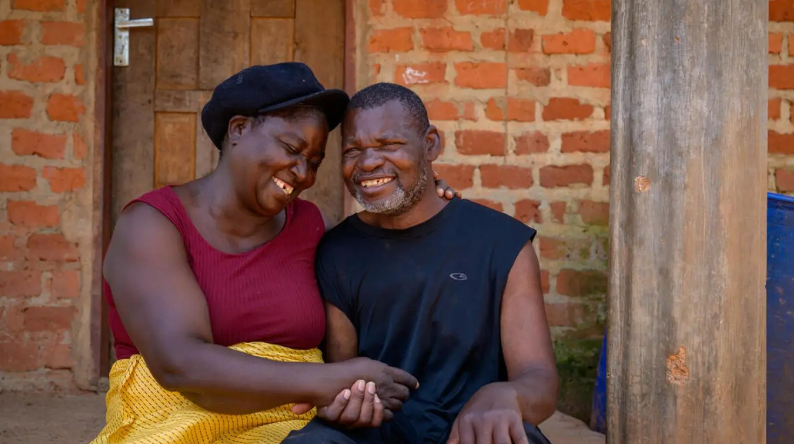 A photo of a man and woman sitting next to each other, gently holding hands and smiling