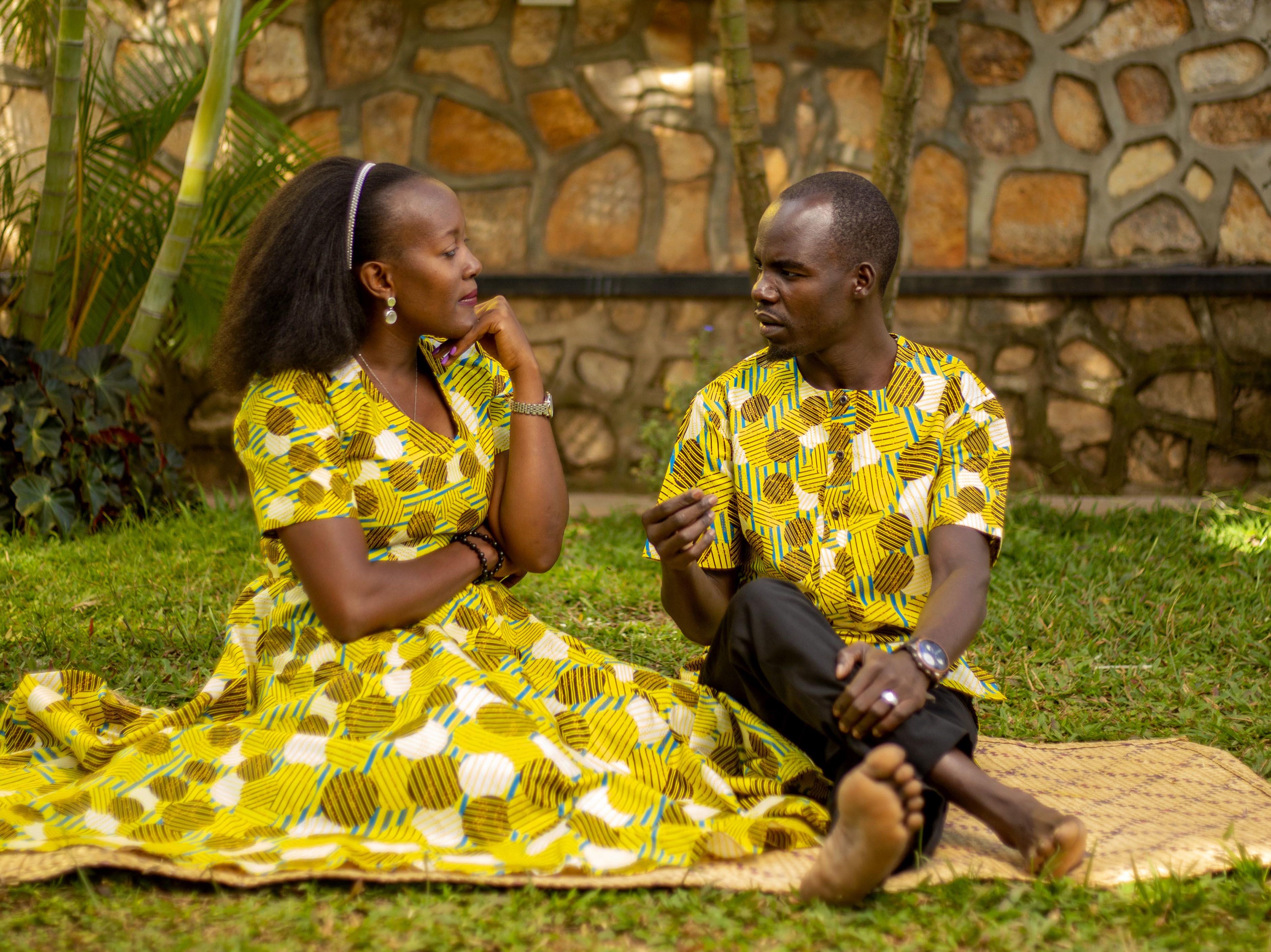 A woman and man are depicted where the man is sitting down with a serious and slightly angry expression on his face, while the woman is standing facing him with her arms crossed looking upset and serious