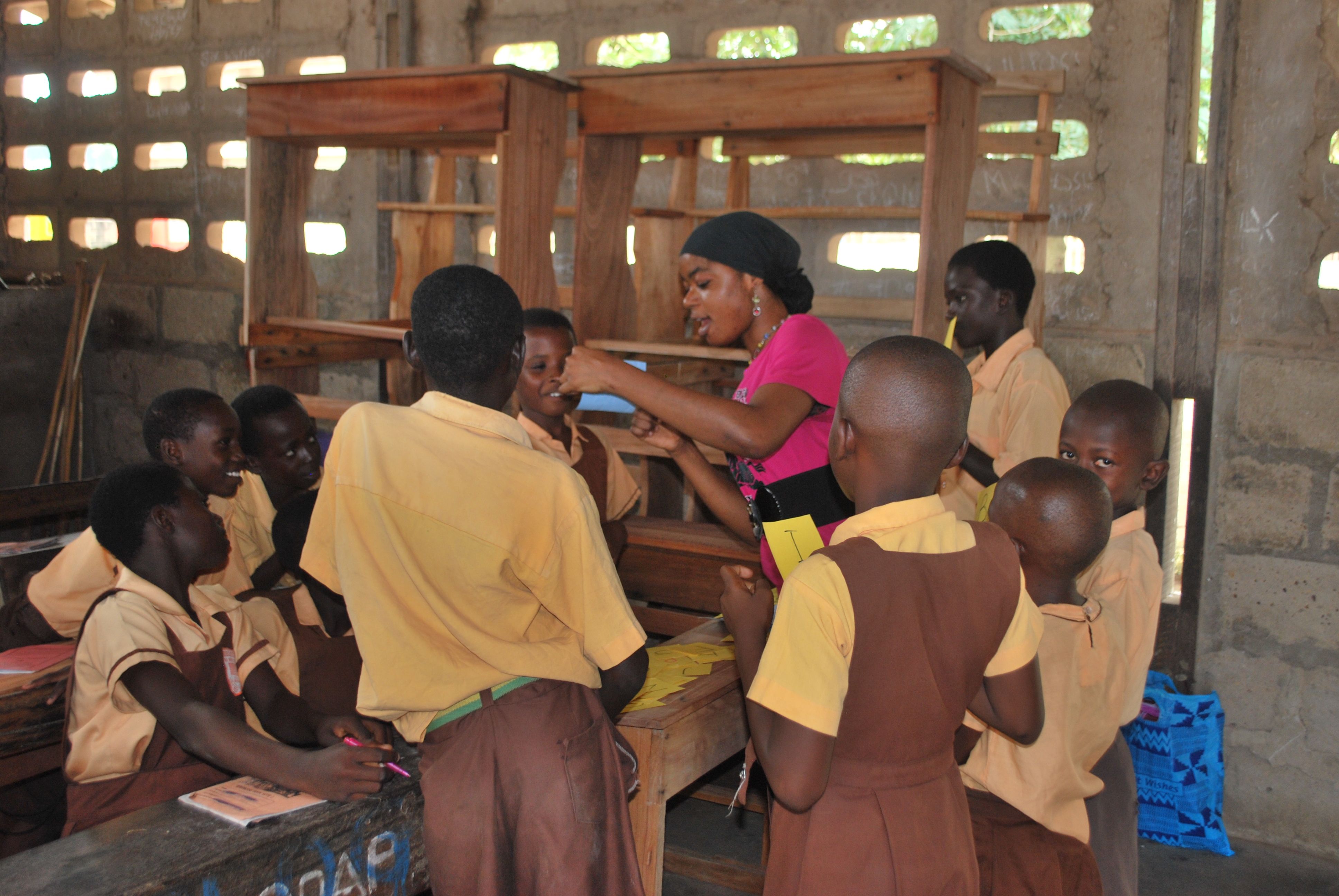 Photo of a classroom where a teacher is standing surrounded by a group of young students.